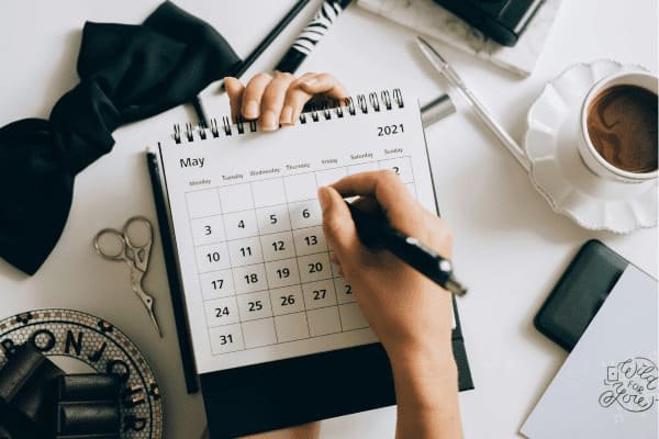 7 hábitos de pessoas organizadas e como adotá-los na sua rotina-mão segurando calendário e caneta sobre a mesa com caneca de café tesoura